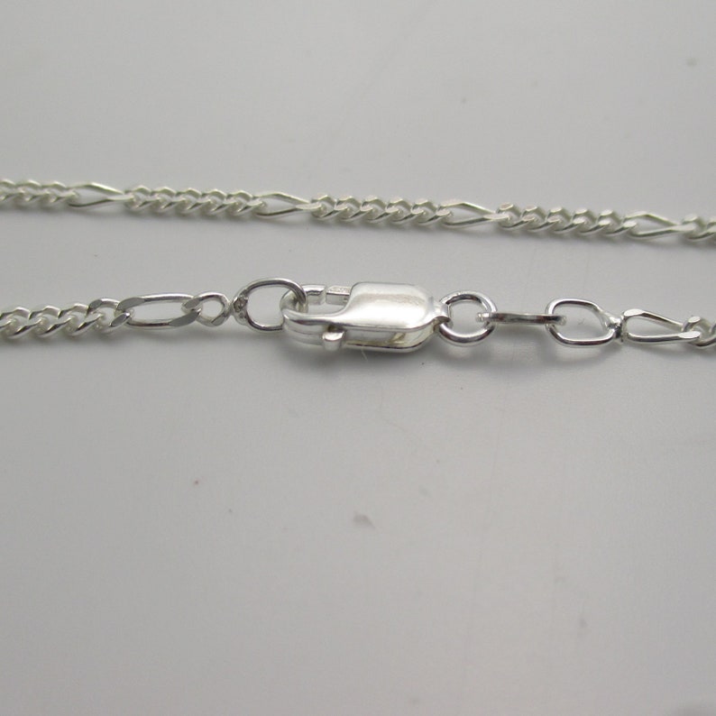 May include: A silver chain necklace with a lobster clasp closure. The chain is a delicate, figaro style.