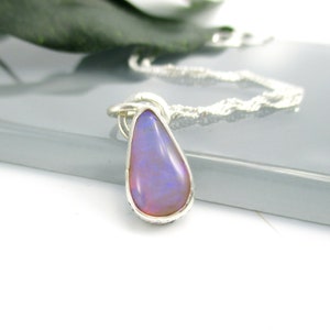 May include: A silver chain necklace with a teardrop-shaped pendant featuring a purple opal gemstone.