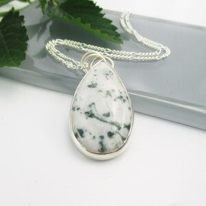 May include: A silver chain necklace with a teardrop-shaped pendant featuring a white and green moss agate stone.