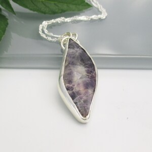 May include: A silver chain necklace with a pendant featuring a large, faceted amethyst gemstone set in a silver bezel. The amethyst is a deep purple color with white inclusions.
