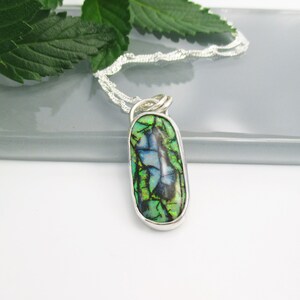 May include: A silver chain necklace with a pendant featuring a green, blue, and black opal stone set in a silver bezel.