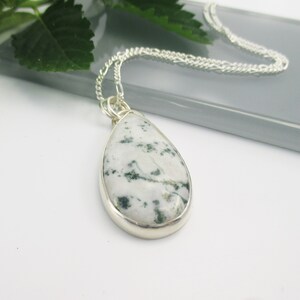 May include: A silver chain necklace with a teardrop-shaped pendant featuring a white and green moss agate stone.