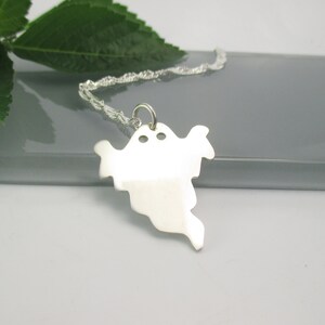 May include: A silver ghost pendant necklace with a chain. The ghost is a simple silhouette with two small holes for eyes.