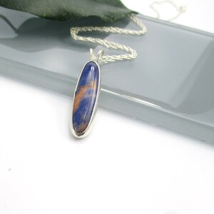 May include: A silver chain necklace with a blue and orange oval pendant. The pendant is made of a natural stone.