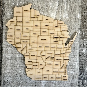 May include: A wooden map of Wisconsin with each county labelled. The map is made of light brown wood and has a rustic, distressed look.