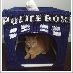 May include: A blue and white knitted cat bed shaped like a TARDIS, a fictional time machine from the British science fiction television series Doctor Who. A ginger cat is sitting inside the bed.