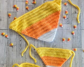 May include: Two crocheted candy corn-themed neck scarves in yellow, orange and white. The larger scarf has a long tie, while the smaller scarf has two shorter ties.