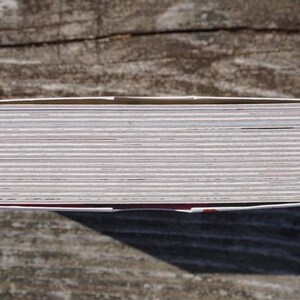 May include: A close-up view of the top of a stack of white cards with a red border. The cards are stacked neatly and are all the same size.