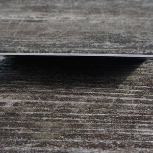 May include: A close-up of a blank, white card with rounded corners. The card is lying flat on a wooden surface.