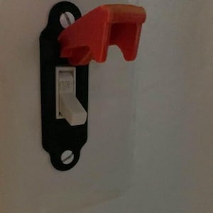 May include: A white light switch with a red plastic safety cover. The cover is in the off position, with the switch lever pointing upwards.