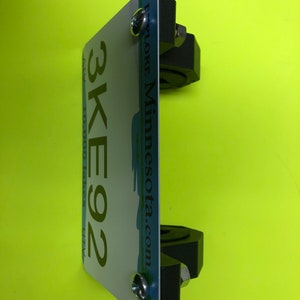May include: A black license plate holder with two silver screws. The license plate is blue and white with the text "Explore Minnesota.com" and the number "3KE92".