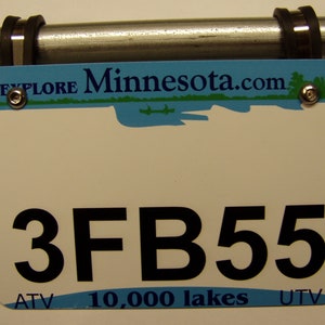 Pu&ograve; includere: Targa bianca con la scritta nera "3FB55", montata su una barra di metallo. La targa ha una sezione superiore blu con "Explore Minnesota.com" e una scena lacustre. La parte inferiore recita "ATV 10.000 laghi UTV".