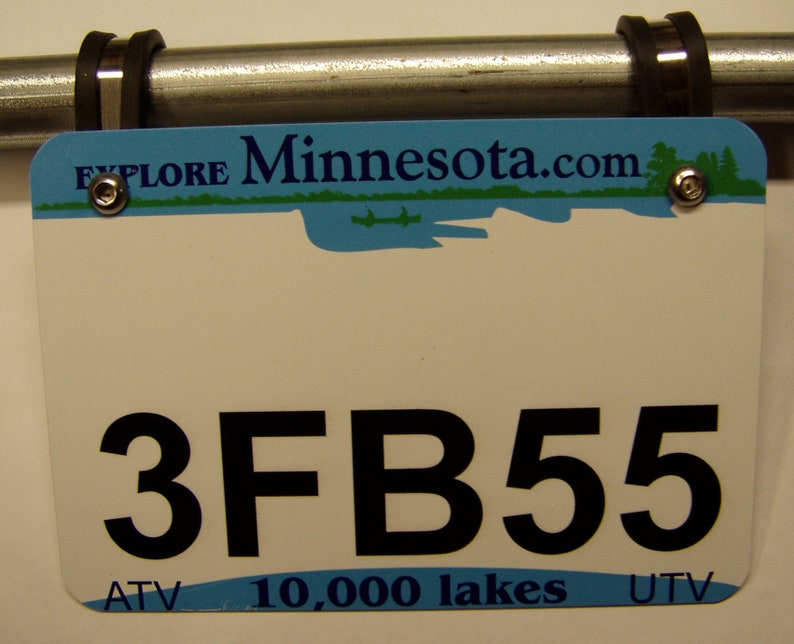 Pu&ograve; includere: Targa bianca con la scritta nera "3FB55", montata su una barra di metallo. La targa ha una sezione superiore blu con "Explore Minnesota.com" e una scena lacustre. La parte inferiore recita "ATV 10.000 laghi UTV".