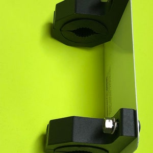May include: A black metal clamp mount with two adjustable clamps and a silver metal plate. The mount is designed to hold a device or object securely.