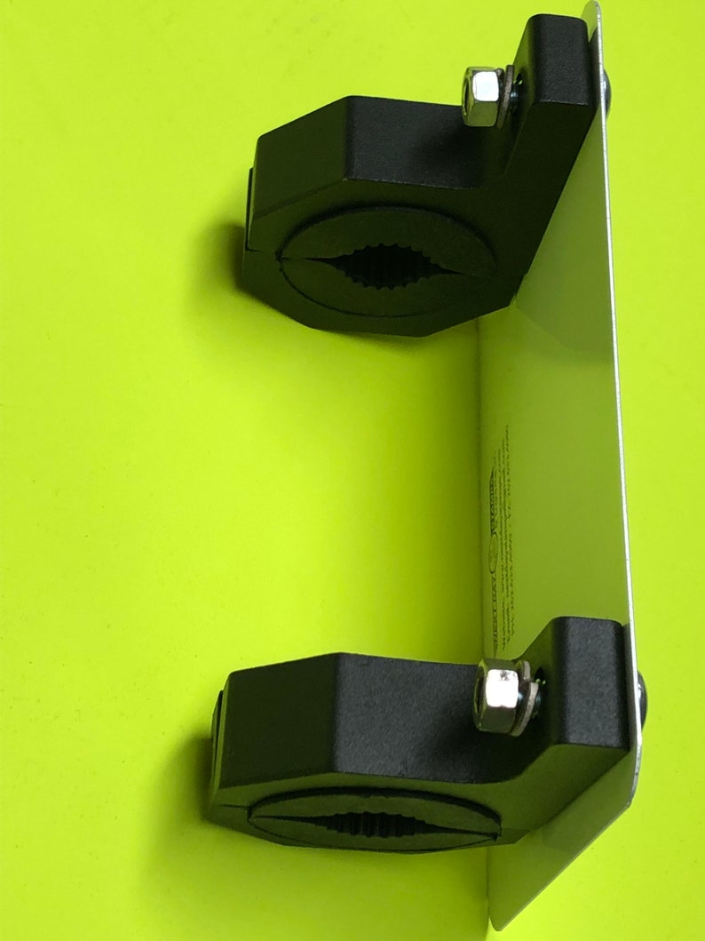 May include: A black metal clamp mount with two adjustable clamps and a silver metal plate. The mount is designed to hold a device or object securely.