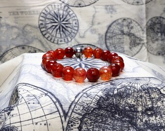 May include: A red agate gemstone bracelet with a silver magnetic clasp. The bracelet is lying on a fabric background with a map design.