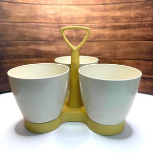 May include: A vintage yellow and white condiment caddy with three compartments. The caddy has a handle and a base. The three compartments are white and the handle and base are yellow. The caddy is made of plastic.