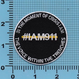 May include: A black and white embroidered patch with a yellow stripe. The text on the patch reads "In the moment of crisis I am the voice within the trenches #IAM911".
