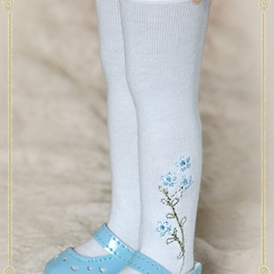 May include: White knee-high socks with a lace trim and blue embroidered flowers. The socks are paired with light blue patent leather shoes with a buckle.