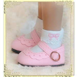 May include: Pink baby shoes with a white strap and buckle. The shoes have a scalloped edge and are decorated with small holes. The shoes are worn with white socks that have a pink bow embroidered on them.