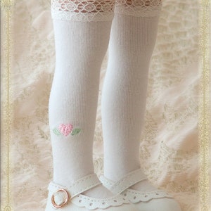May include: White knee-high socks with a lace trim and a pink heart embroidered on one sock. The socks are paired with white shoes with a buckle.