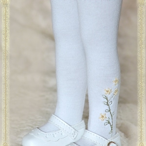 May include: White knee-high socks with a floral embroidery design and white lace trim. The socks are paired with white leather shoes with a buckle.