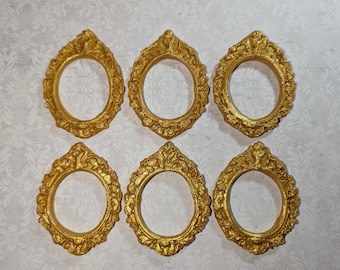 May include: Six ornate, gold-colored oval picture frames. Each frame has a detailed, textured design around the edges. The frames are arranged in two rows of three on a patterned background.