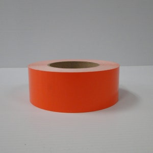 May include: A roll of bright orange reflective tape. The tape is wound around a cardboard core.