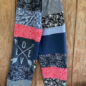 May include: Patchwork pants with a variety of patterns, including leopard print, black and white stripes, and a red geometric design. The word "LOVE" is printed on the left leg. The pants are hanging on a clothesline.