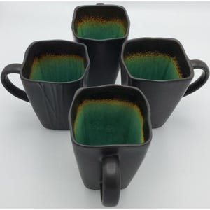 May include: A set of four square-shaped mugs with matte black exteriors and a vibrant teal interior glaze that transitions to a warm brown rim. Each mug features a sturdy handle and a distinct, slightly irregular, organic silhouette.