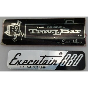 May include: Two rectangular metal labels. The top label is black with silver text reading THE ORIGINAL Trav-L-Bar TM by Ever-Wear and a cartoon suitcase character. The bottom label is silver and black with the text Executair 880 and U.S. PAT. 3,171,700.