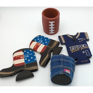 Könnte beinhalten: Eine Sammlung von vier Getränkeisolatoren, darunter eine braune, fußballförmige Hülle mit weißen Schnürsenkeln, zwei stiefelförmige Hüllen mit amerikanischem Flaggendesign und DurangoBoots.com-Text, eine blaue Jeanshülle und eine blaue Trikot-Flaschenhülle.