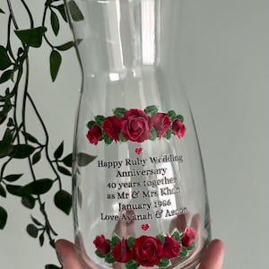 May include: A clear glass jug with a curved shape, decorated with red roses and text. The text says "Happy Ruby Wedding Anniversary 40 years together as Mr & Mrs Khan January 1986 Love Ayanah & Azaan."