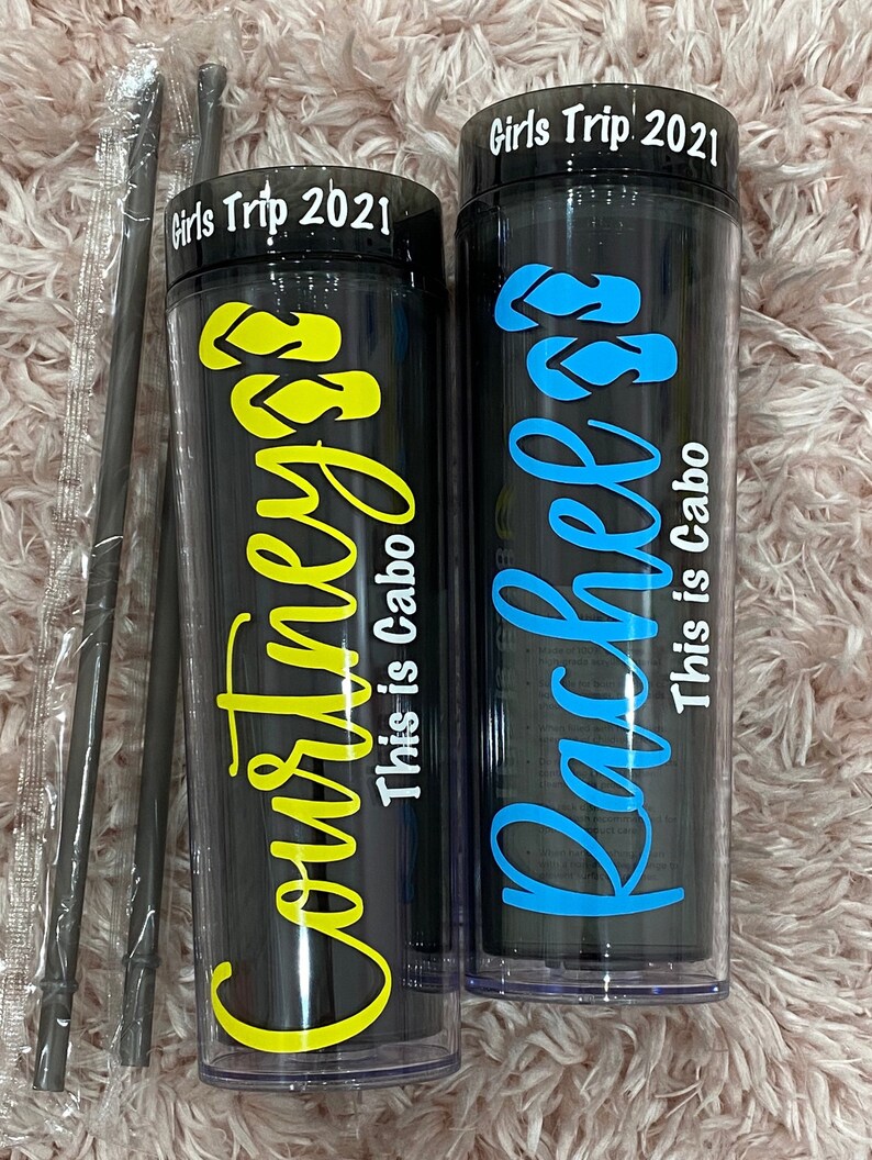 Peut inclure: Deux gobelets en plastique noir et transparent avec couvercles et pailles. Les gobelets portent le texte "Girls Trip 2021" en haut et les noms "Courtney" et "Rachel" en lettres jaunes et bleues. Le texte "This is Cabo" est &eacute;crit sous les noms.