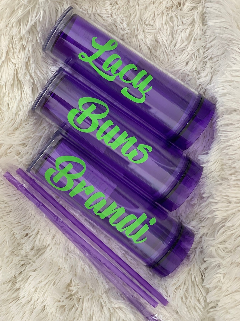 Peut inclure: Trois gobelets violets avec couvercles et pailles. Les gobelets portent des inscriptions vertes qui disent "Brandi", "Burns" et "Lacy".