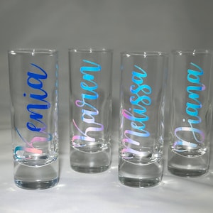 Puede incluir: Cuatro vasos de chupito de vidrio transparente con letras iridiscentes azules y rosas. Los nombres "Benicia", "Katelyn", "Melissa" y "Diana" est&aacute;n escritos en los vasos.