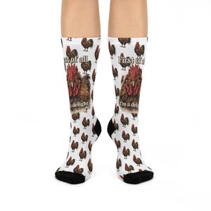 May include: White socks with a repeating pattern of brown roosters. The socks feature a large rooster graphic with the text "First of all, I'm a delight." Black heels and toes complete the design. These socks are a fun accessory.