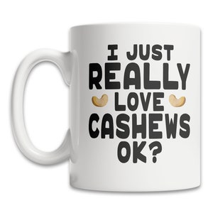 May include: White ceramic coffee mug with black text that reads "I just really love cashews ok?" with two cashew nut illustrations.