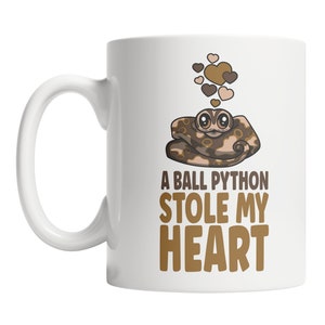 May include: White ceramic coffee mug with a brown and tan cartoon ball python with hearts above it. The text "A ball python stole my heart" is printed in brown on the mug.