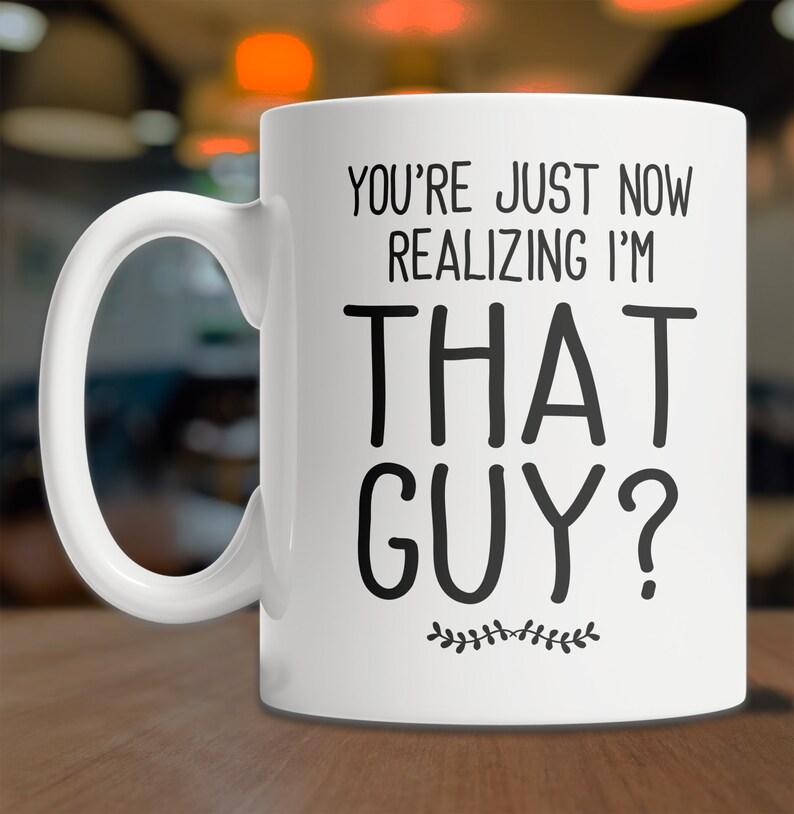 May include: White ceramic coffee mug with black text that reads "You're just now realizing I'm that guy?" with a small decorative vine design at the bottom.