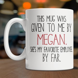 May include: White ceramic mug with black text that reads "This mug was given to me by Megan. She's my favorite employee by far."