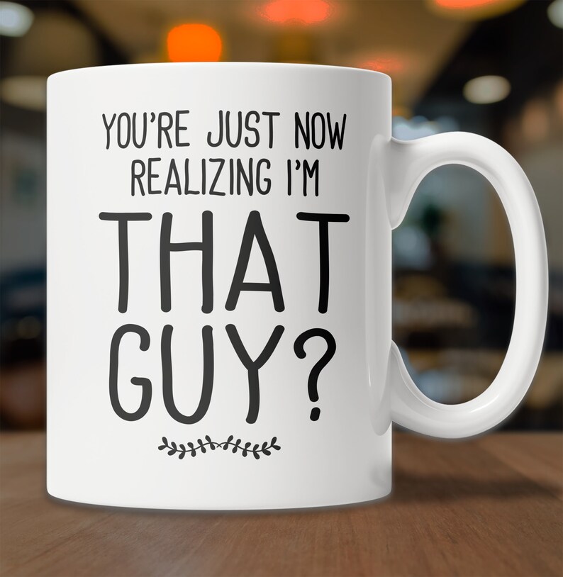 May include: White ceramic coffee mug with black text that reads "You're just now realizing I'm that guy?" with a small decorative leaf design at the bottom.