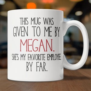 May include: White ceramic coffee mug with black text that reads "This mug was given to me by Megan. She's my favorite employee. By far."