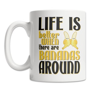 May include: White ceramic coffee mug with a black and yellow design. The mug reads "Life is better when there are bananas around". Two cartoon bananas are depicted on the mug.