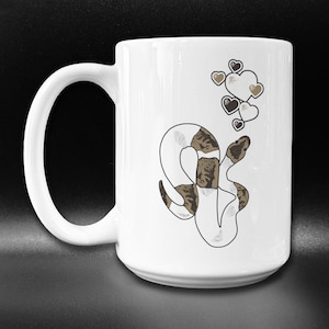May include: White ceramic coffee mug with a black and white snake design and a cluster of brown hearts floating above the snake.