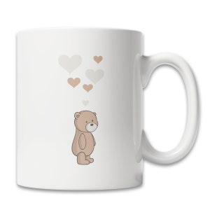 May include: White ceramic mug with a brown teddy bear illustration and a design of brown and white hearts floating above the bear.