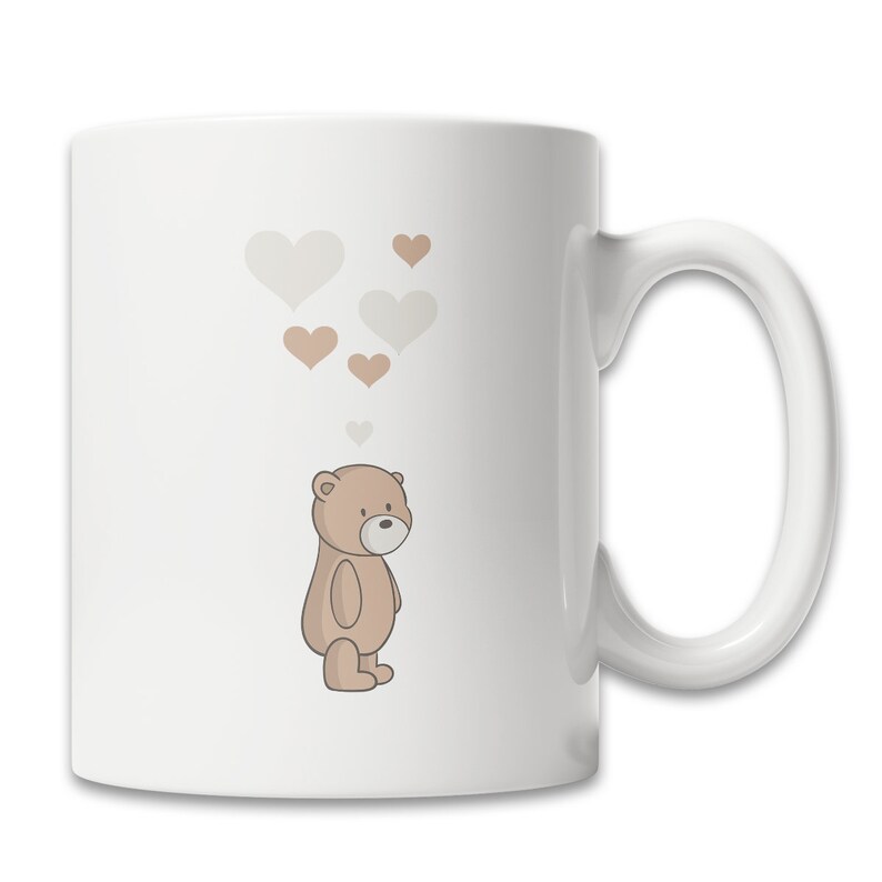 May include: White ceramic mug with a brown teddy bear illustration and a design of brown and white hearts floating above the bear.