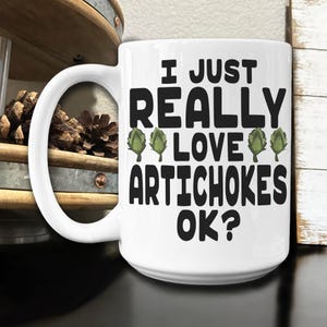 May include: White ceramic coffee mug with a black graphic that reads "I just really love artichokes ok?" with three green artichoke illustrations.