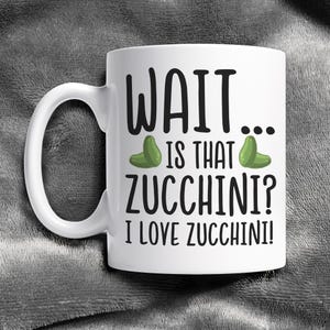 May include: White ceramic coffee mug with a black and green design. The mug says "WAIT... IS THAT ZUCCHINI? I LOVE ZUCCHINI!"