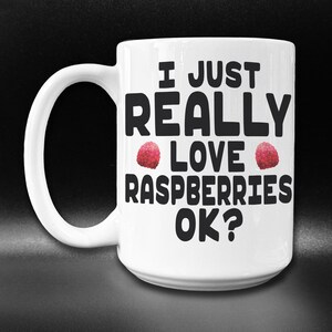 May include: White ceramic coffee mug with a black graphic that reads "I just really love raspberries ok?" with two red raspberries on either side of the word "love".